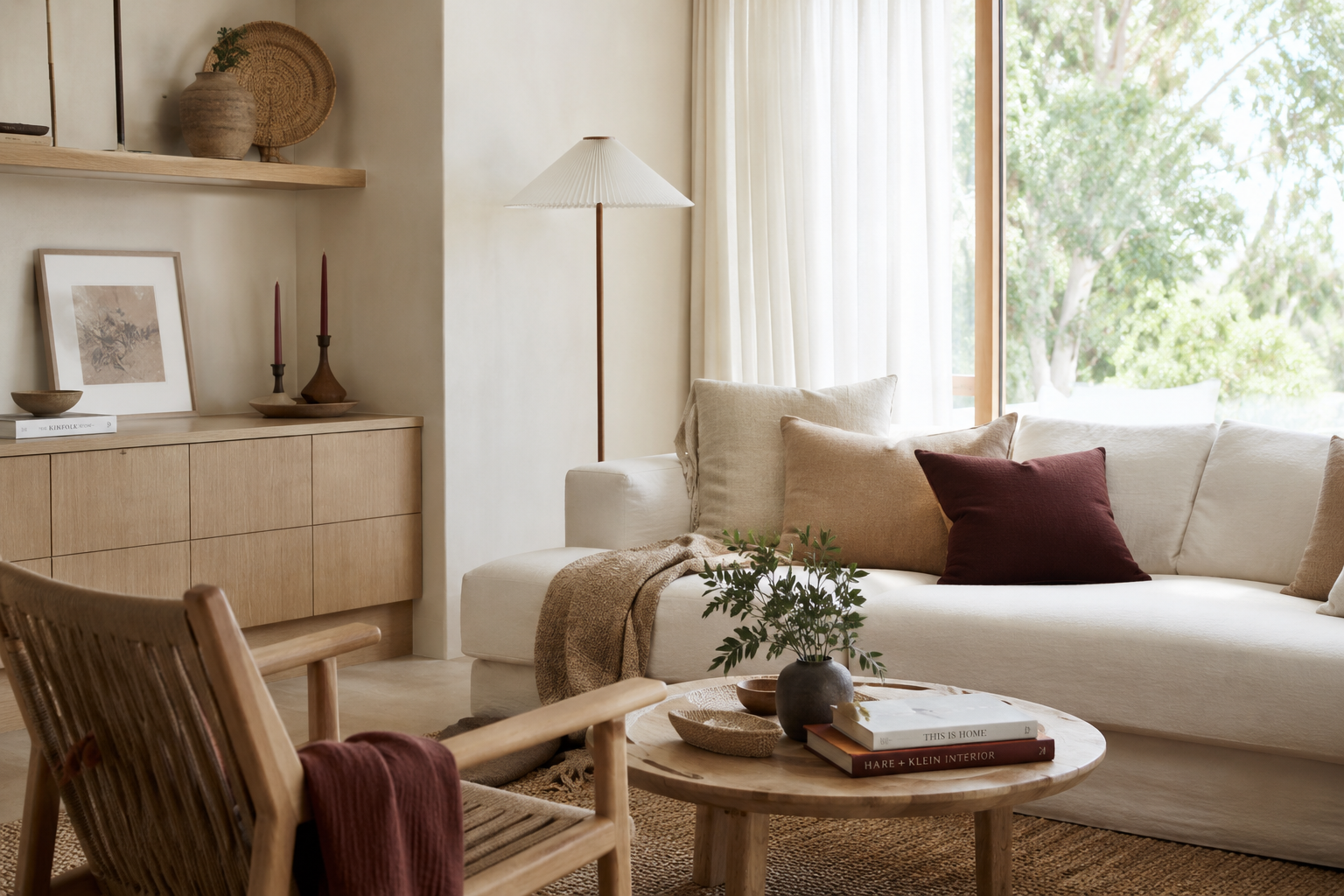 Bright organic modern Japandi living room with a cream sofa, natural wood furniture, burgundy pillows and taper candles, layered neutral textiles, and minimal fall decor.
